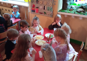 dzieci siedzą przy stoliku i jedzą poczęstunek