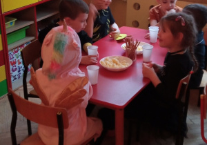 dzieci siedzą przy stoliku i jedzą poczęstunek