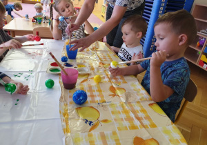 Zdjecie od przodu na dzieci siedzące przy stole i malujące farbami 