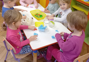 Dzieci siedzą przy stoliku i robią kulki z bibuły