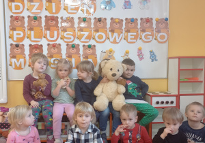 Dzieci pozują do zdjęcia przy dekoracji na tablicy z okazji Dnia pluszowego misia