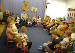 Dzieci siedzą na krzesełkach w kole słuchając bajki