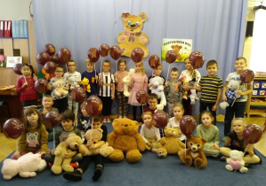 Dzieci stoją w grupie z misiami oraz balonami