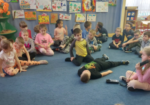 Dzieci siedzą na dywanie i oglądają sceny odgrywane przez dzieci
