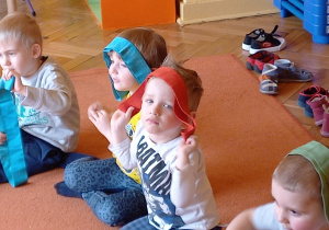 Dzieci siedzą na dywanie z szarfami na głowie