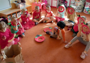 Dzieci siedzą na dywanie o trzymaja papierowe maski