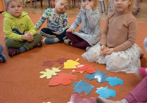 Dzieci siedzą na dywanie I bawią się papierowymi liśćmi