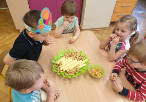 Dzieci jedzą chrupki i ciastka przy stole