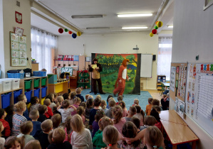 Dzieci oglądają przedstawienie w przedszkolu siedząc na dywanie