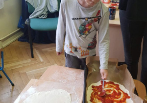 Chłopiec smaruje sosem ciasto na pizze