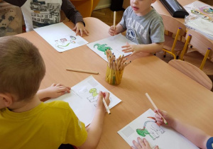 Dzieci przy stoliku kolorują obrazki z dinozaurami