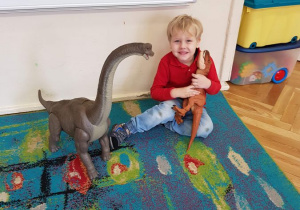 Chlopiec pozuje do zdjecia z zabawkowymi dinozaurami.