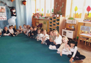 Dzieci w eleganckich strojach siedzą na dywanie.