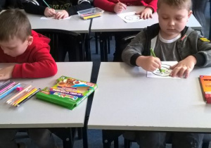 Dzieci siedzą przy stolikach i kolorują buzie