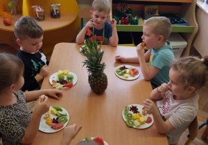 Dzieci siedzą przy stolikach i jedzą owoce egzotyczne