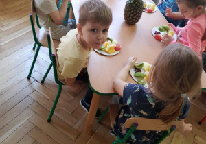 Dzieci przy stole jedzą pokrojone owoce egzotyczne