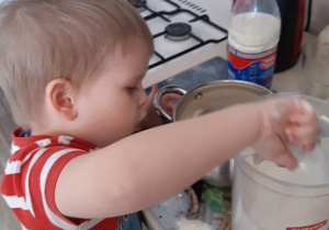 Chłopiec pomaga mamie w kuchni dosypując mąkę do ciasta