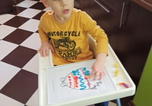 Chłopiec wykleja pisankę bibułą