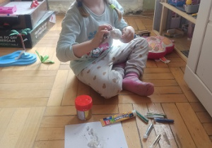Dziewczynka siedzi na podłodze i ozdabia styropianowe pisanki brokatem
