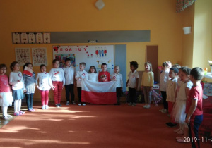 Dzieci stoja w półkolu i trzymają flagę Polski