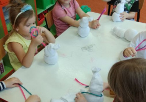 Dzieci siedzą przy stoliku i wykonują bałwanki z białej skarpetki i sizalu