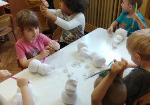 Dzieci siedzą przy stoliku i wykonują bałwanki z białej skarpetki i sizalu