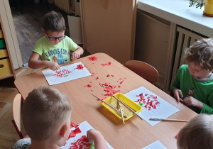 dzieci przy stole przyklejają czerwone kawałki papieru na pomidorka