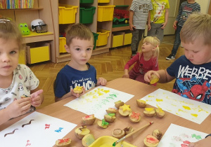 dzieci siedzą przy stole i odbijają stemple z ziemniaków na kartce