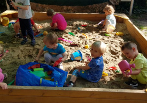 Dzieci bawią się w piaskownicy - widok na całą piaskownicę.