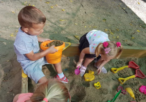 Dwójka dzieci siedzi w rogu piaskownicy.