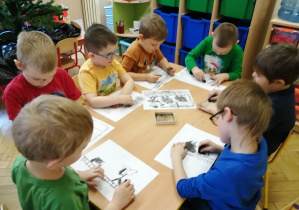 dzieci siedzą przy stolikach i rysują węglem