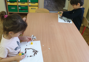 Dzieci siedzą przy stole i wyklejają prace kolorowym papierem