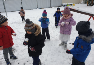 Dzieci zbierają śnieg łyżeczkami do miseczek