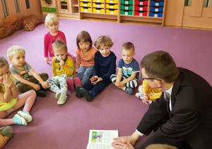 Dzieci siedzą w kole na dywanie i słuchają czytanej bajki