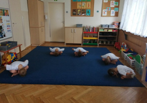 Dzieci wykonują skłony w przód na siedząco.