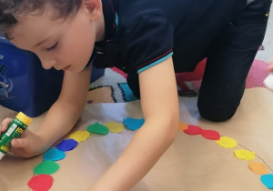 Chłopiec przykleja kolorowe kółka na karton