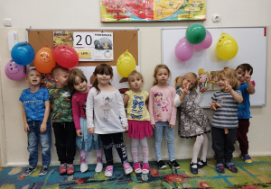 Dzieci stoją przy tablicy z balonami