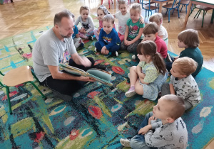 Dzieci siedzą na dywanie i słuchają czytanej bajki