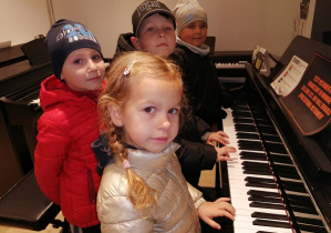 Dzieci stoją przy keybordzie i próbują na nim grać.
