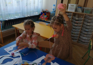 Dziewczynki wykonują pracę plastyczną papierową gitarę