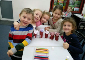 Dzieci przy stoliku pokazują swoje prace plastyczne