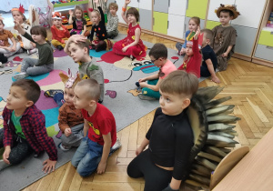 Dzieci siedzą na dywanie przed tablicą multimedialną