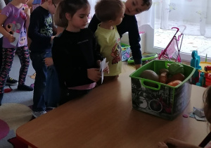 Dzieci stoją w kolejce i wybierają owoce do kupienia za zabawkowe pieniadze