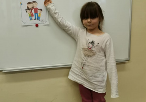 Dziewczynka stoi przy tablicy i wskazuje obrazek